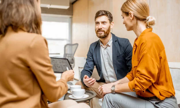 Photo d'une agent immobilier présentant un bien immobilier à deux clients sur une tablette portable.